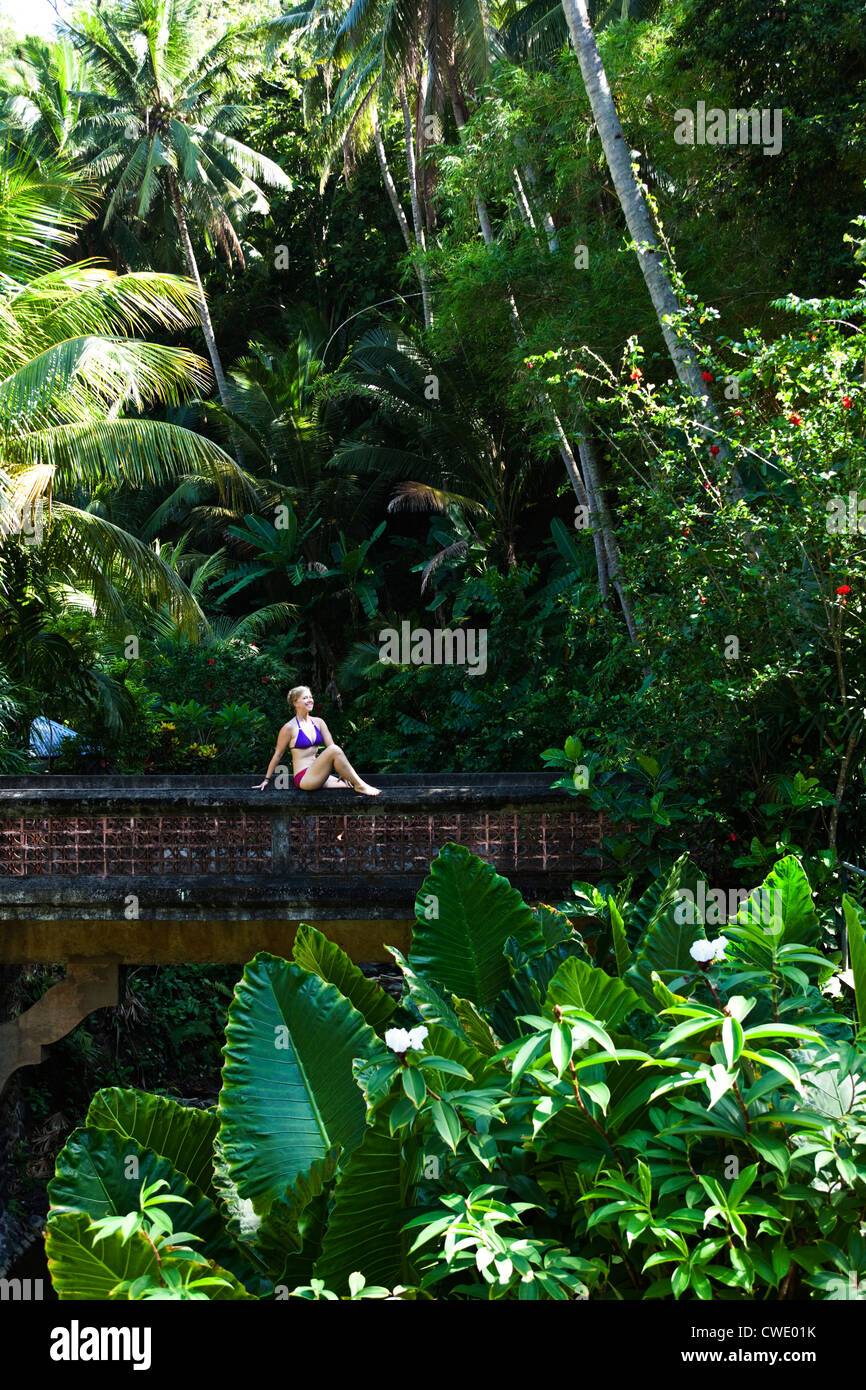 Une belle femme se détendre sur un pont à côté d'un hot springs entouré par une jungle luxuriante et des fleurs à Bali, Indonésie. Banque D'Images