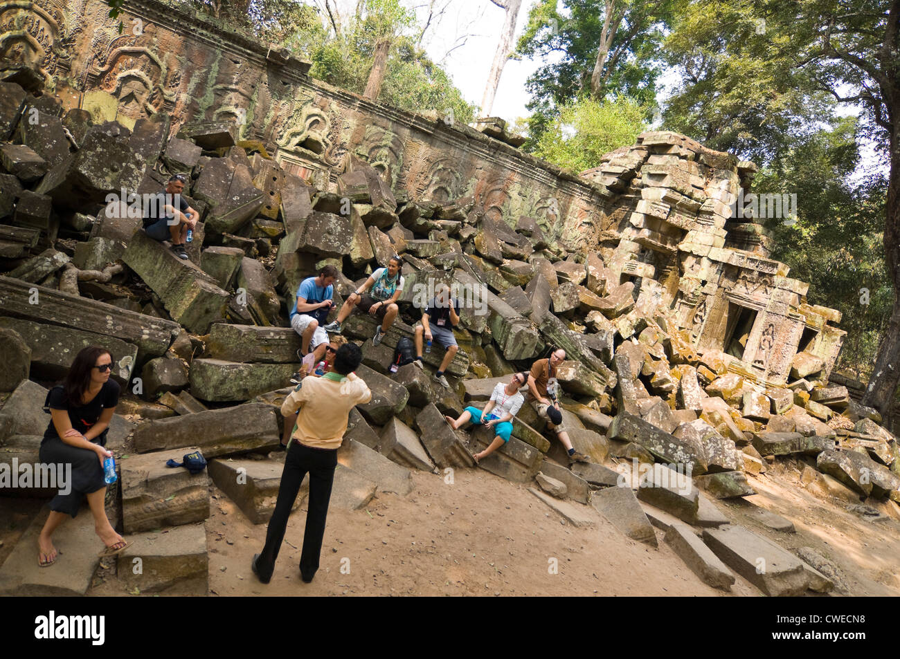 Vue horizontale de touristes assis sur les ruines d'un mur avec un guide à Ta Prohm temple Tomb Raider ou à Angkor Thom. Banque D'Images