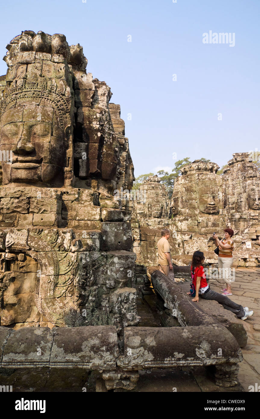 Vue en gros plan vertical de l'énorme en pierre de visages du Bayon temple avec les touristes de prendre des photographies à Siem Reap. Banque D'Images