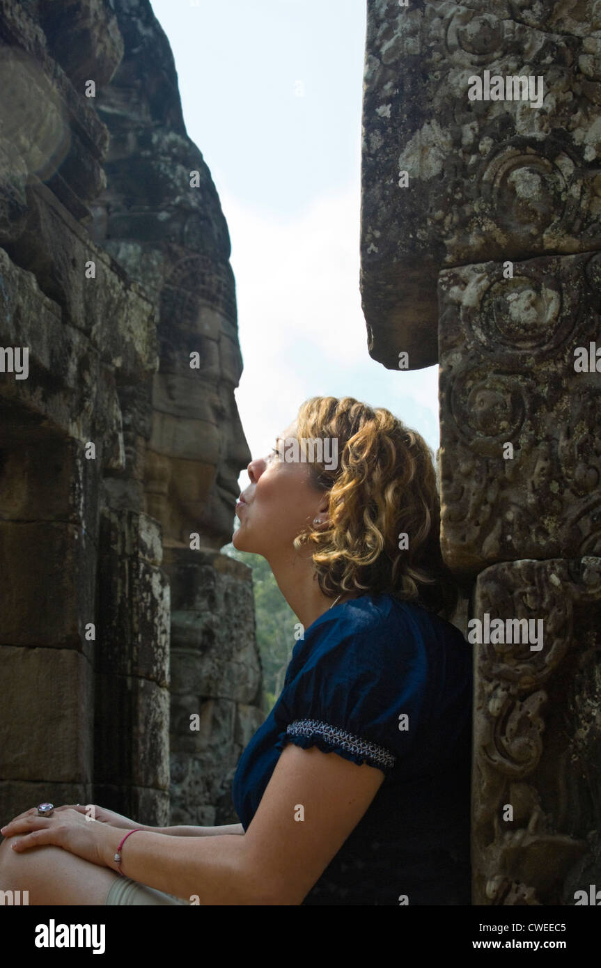 Portrait d'une verticale de tourisme de l'Ouest faisant semblant d'embrasser l'un des nombreux visages sculptés au temple Bayon à Siem Reap. Banque D'Images