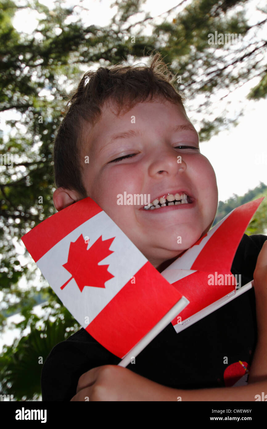 Un sourire fier et acclamer six ans garçon agitant des drapeaux patriotiques l'occasion de la fête du Canada Banque D'Images