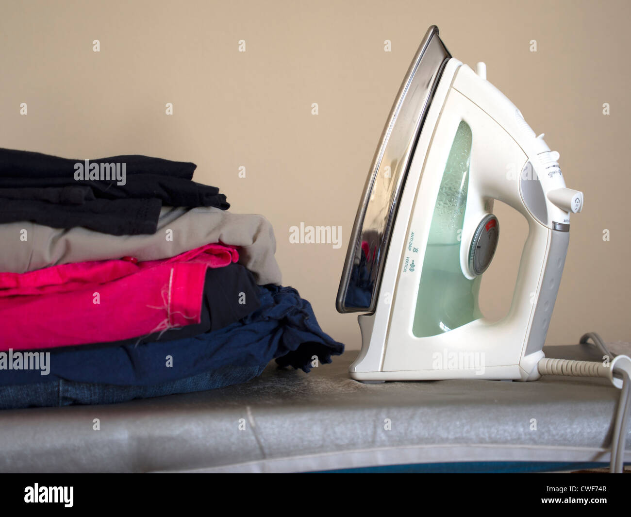 Un tas de planche sur la planche à repasser. Un fer à vapeur attend d'être utilisé. Banque D'Images