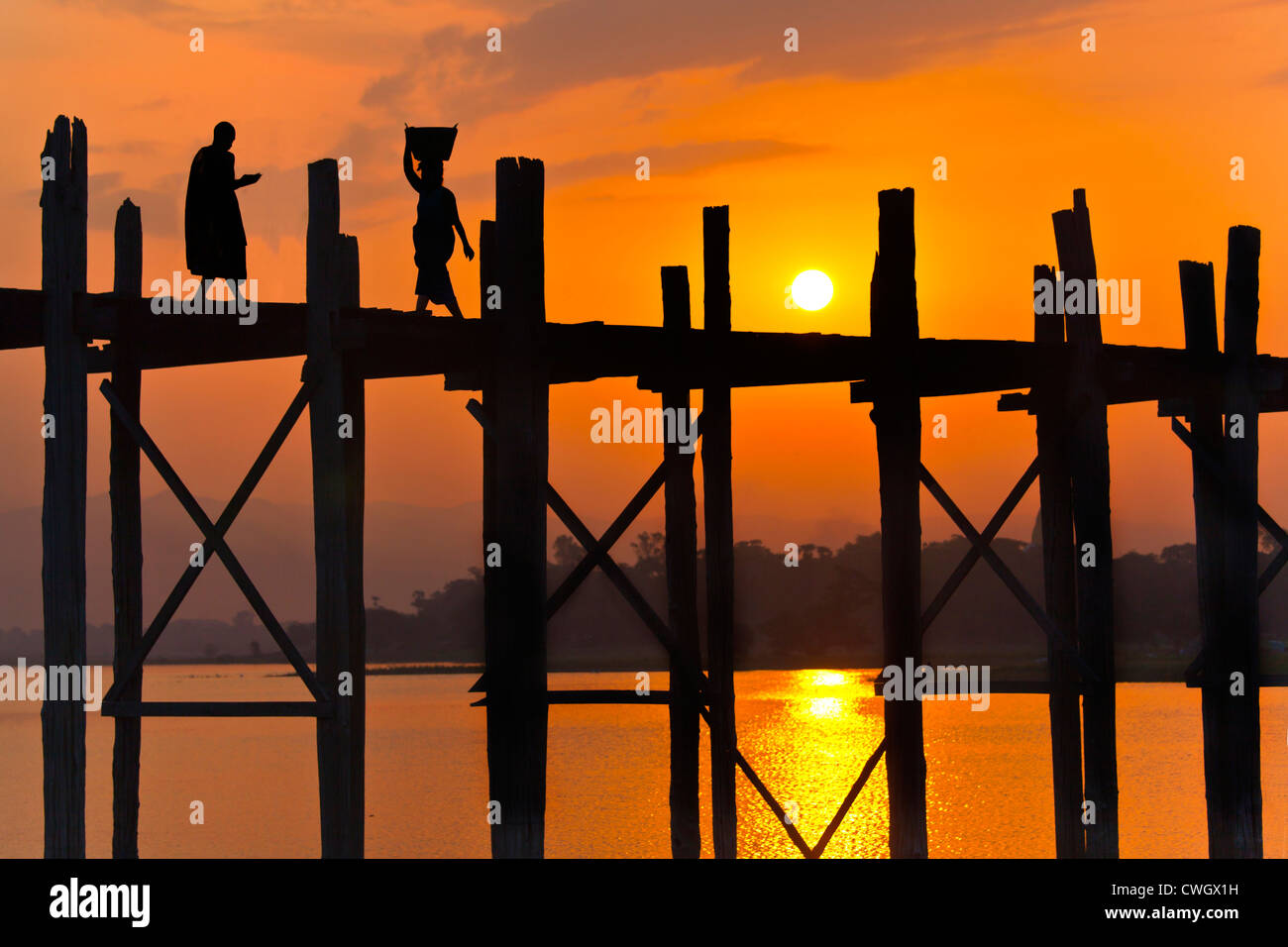 Les Birmans utilisent le pont en teck U BEINS de commuer à travers le lac Taungthaman au lever du soleil - AMARAPURA, MYANMAR Banque D'Images