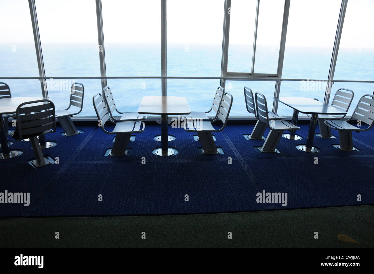 Tables et chaises en acier vide, fixé sur le pont, la fenêtre du sol au plafond, vue sur la mer, sol bleu foncé, cruise ferry, Golfe de Gascogne. Banque D'Images