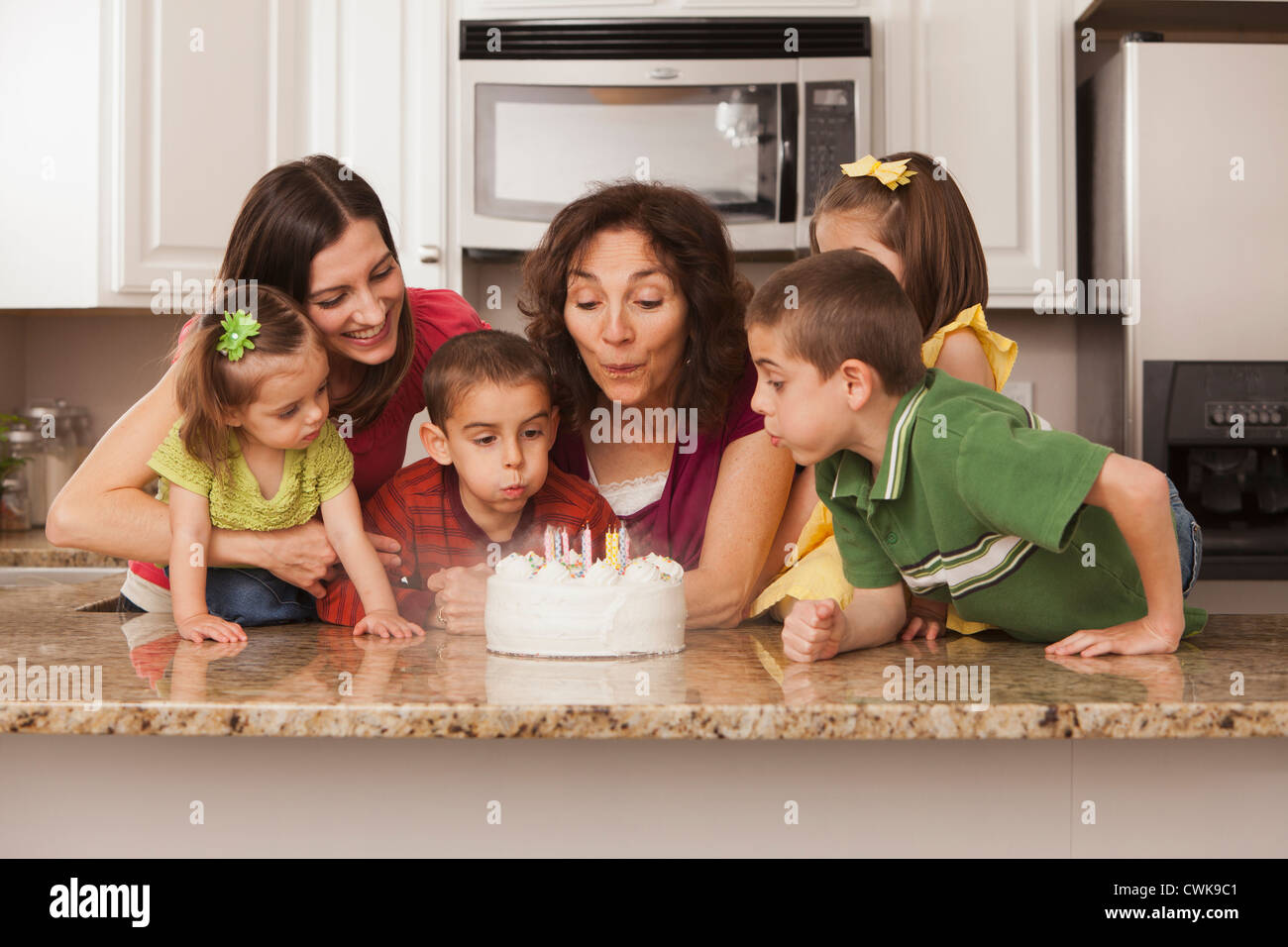 La famille de race blanche dans la cuisine qui sort du gâteau d'anniversaire Banque D'Images