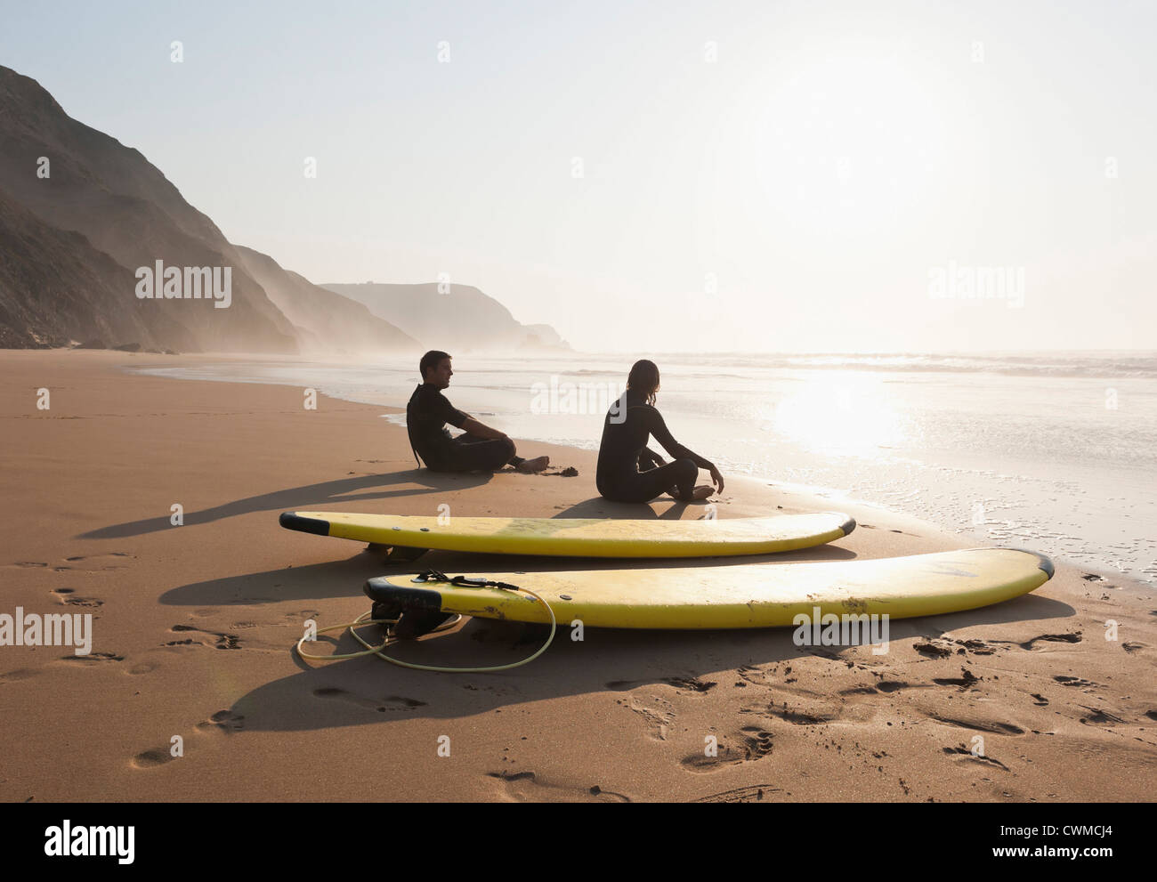 Le Portugal, Couple sitting on beach par surfboard Banque D'Images
