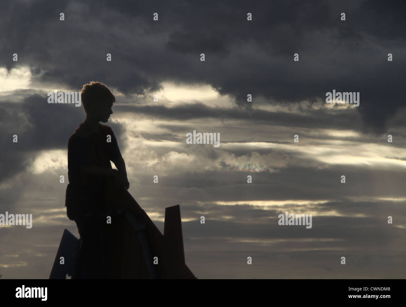 Garçon sur le toit de l'armature du parc avec ciel dramatique. Banque D'Images
