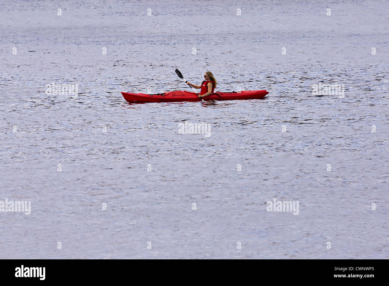 Fille aux cheveux blonds portant des lunettes et gilet rouge dans une pagaie kayak rouge dans l'eau ouverte. Banque D'Images