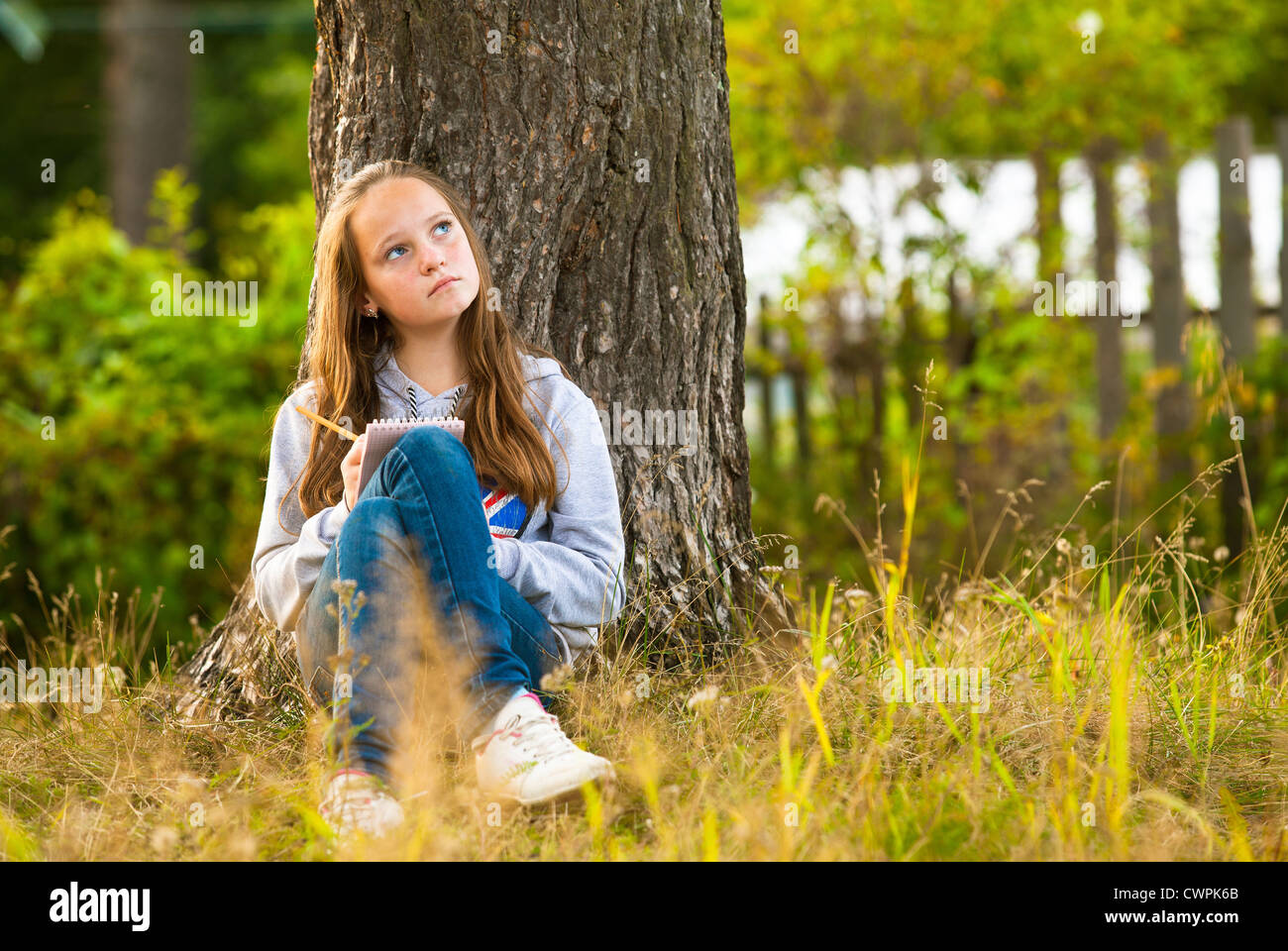 Belle teen girl écrit dans un ordinateur portable tout en restant assis dans le parc (regarde rêveusement) Banque D'Images