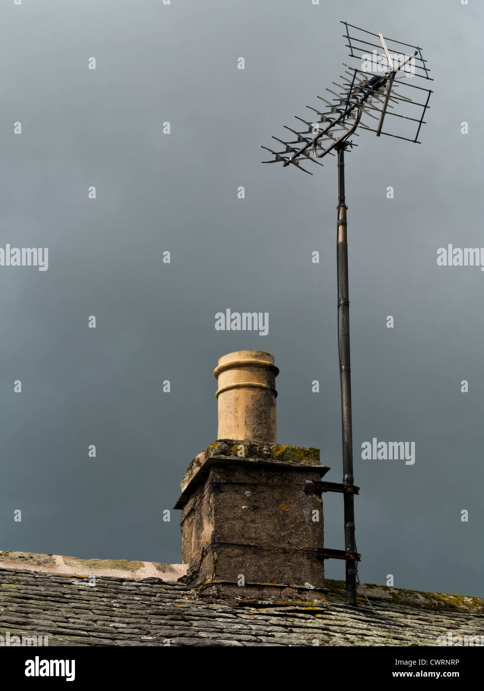 Gîte rural la section de cheminée en pierre et un toit en ardoise avec antenne de télévision contre un sombre ciel couvant Banque D'Images