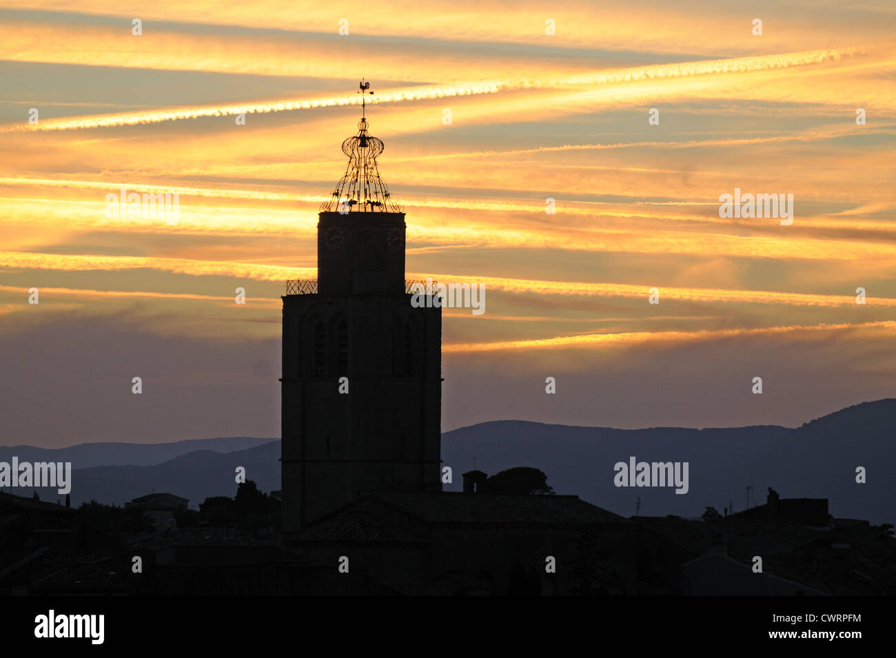 Tour de l'église St Gervais et cage bell silhouetté contre ciel coucher de soleil spectaculaire avec jet trails Caux Languedoc Roussillon France Banque D'Images