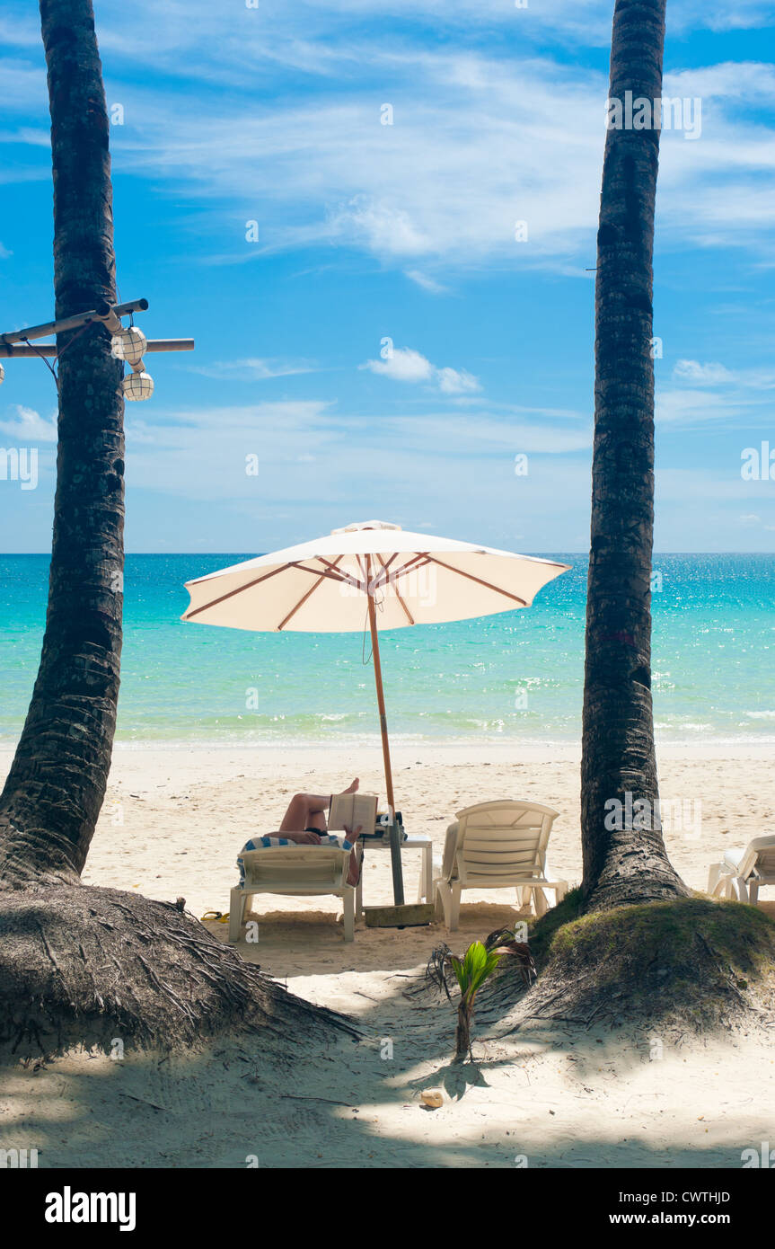 Quelqu'un lisant un livre sous un parasol blanc sur un tropica beach Banque D'Images