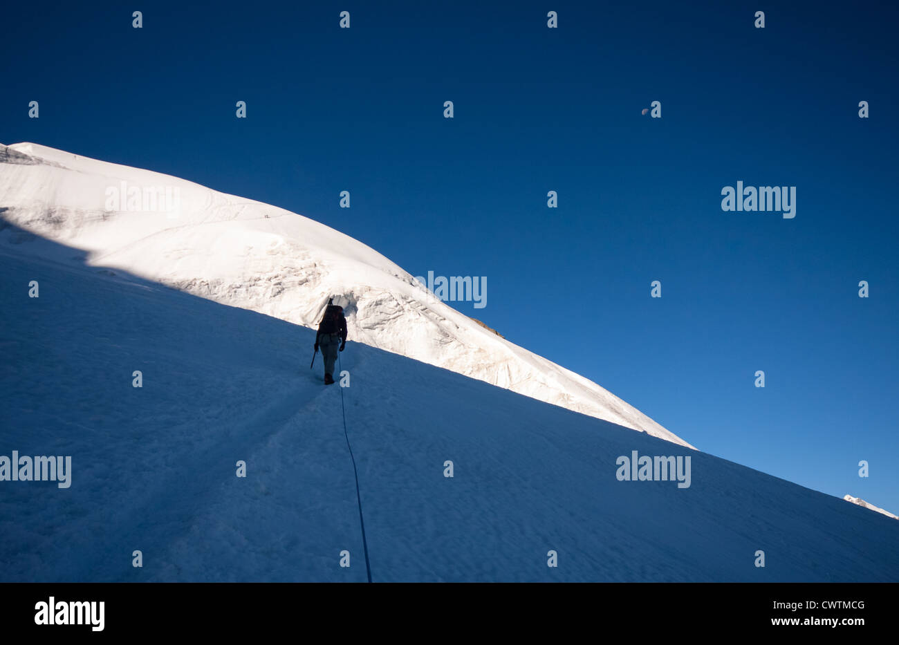 L'alpiniste monte sur le bas des pentes ombragées de Weissmies comme la lumière du soleil de l'avant des approches d'entre eux. Banque D'Images