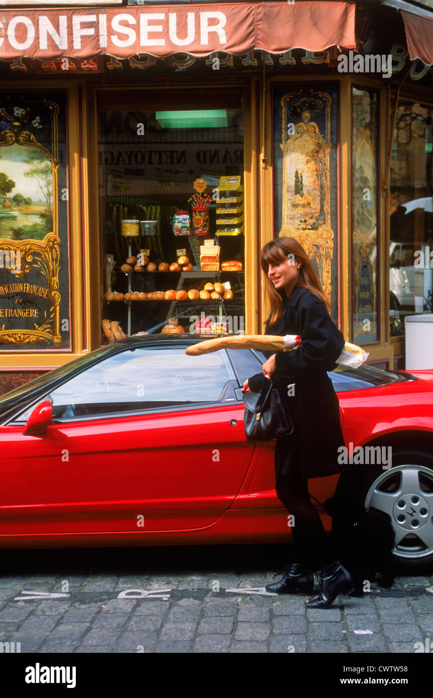 Femme à Paris baguette boulangerie laissant entrer dans cher voiture sport rouge avec caniche français sur cobblestone street Banque D'Images