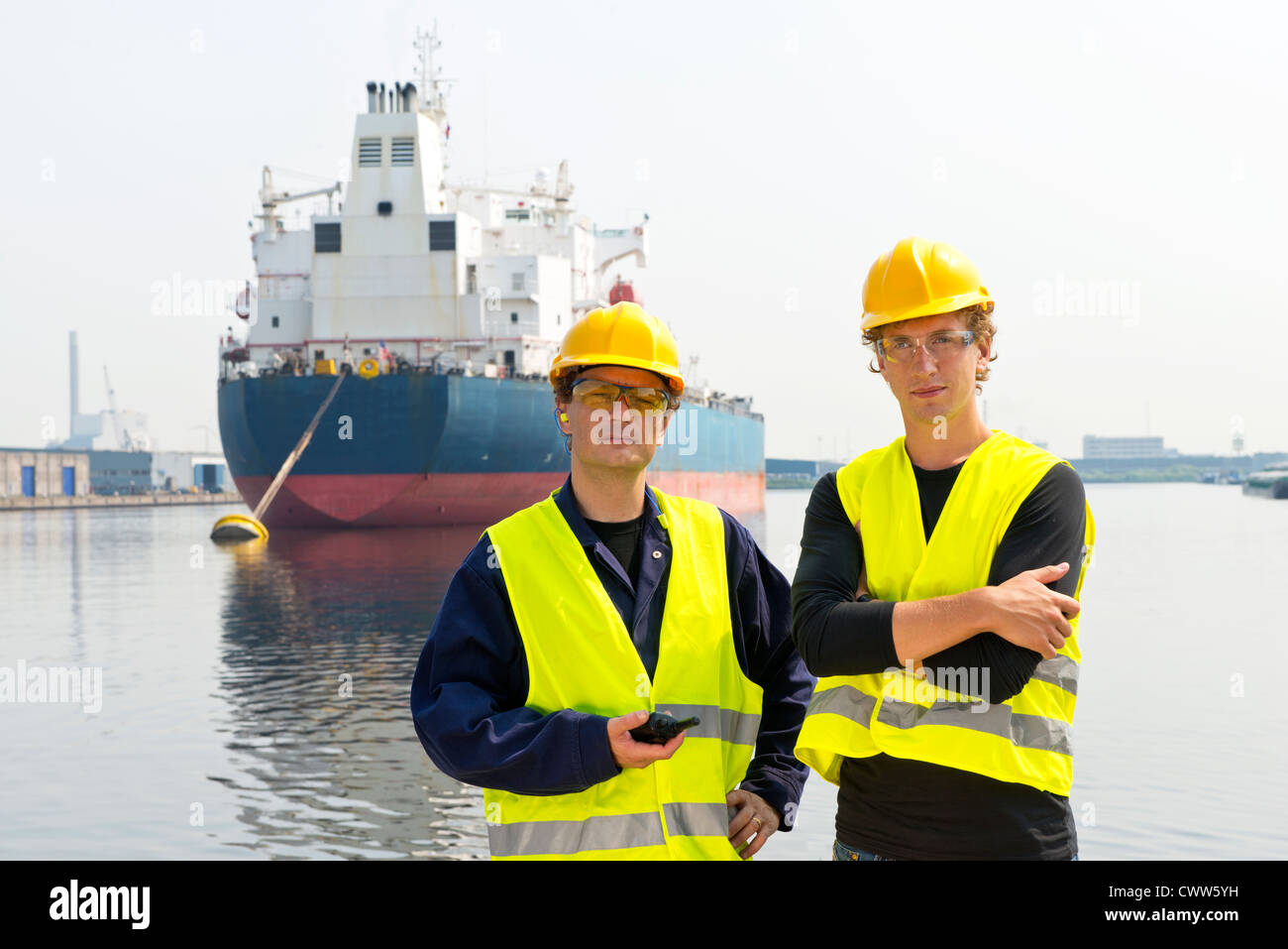 Portrait de deux dockers, posant devant un grand pétrolier amarré dans un port industriel Banque D'Images