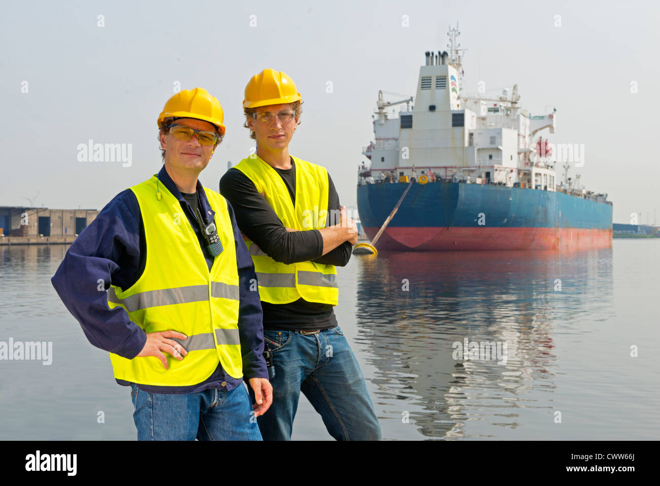 Deux dockers posant en face d'un grand pétrolier, dans un port industriel Banque D'Images