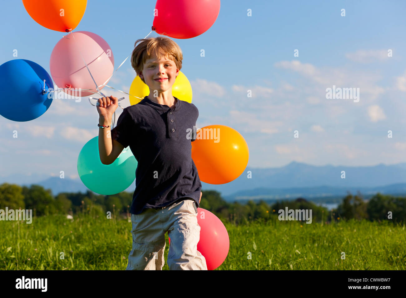 Garçon avec des ballons colorés dans l'herbe Banque D'Images