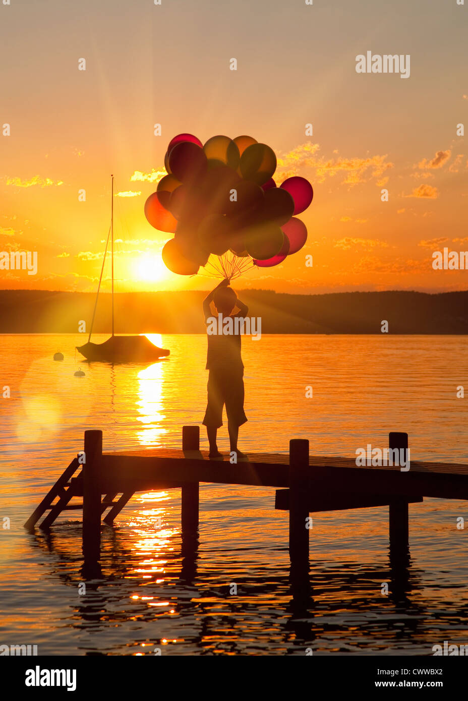 Boy holding balloons on wooden dock Banque D'Images