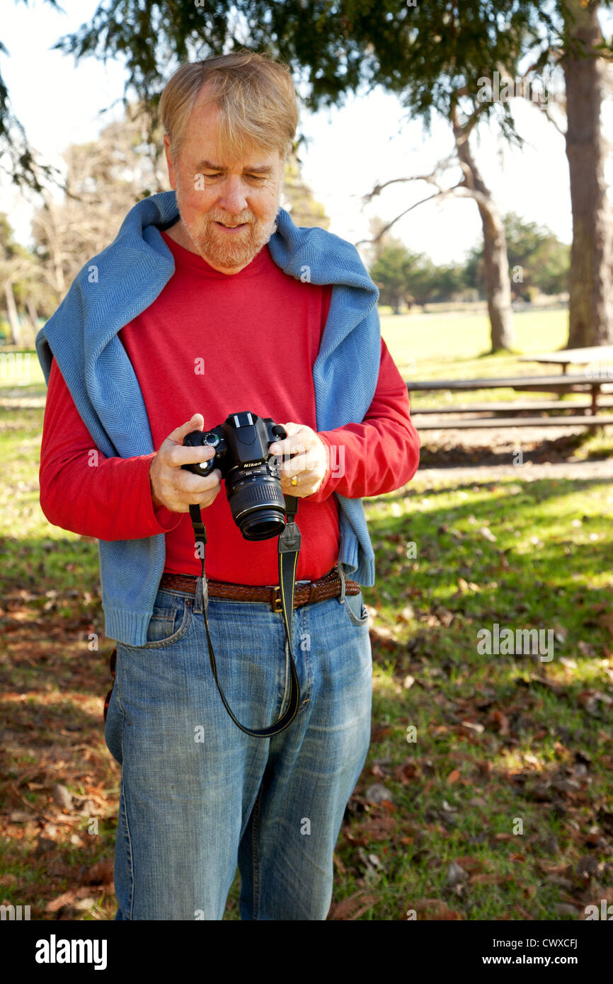 Un homme dans son 60's est debout à l'extérieur tenant une caméra. Banque D'Images