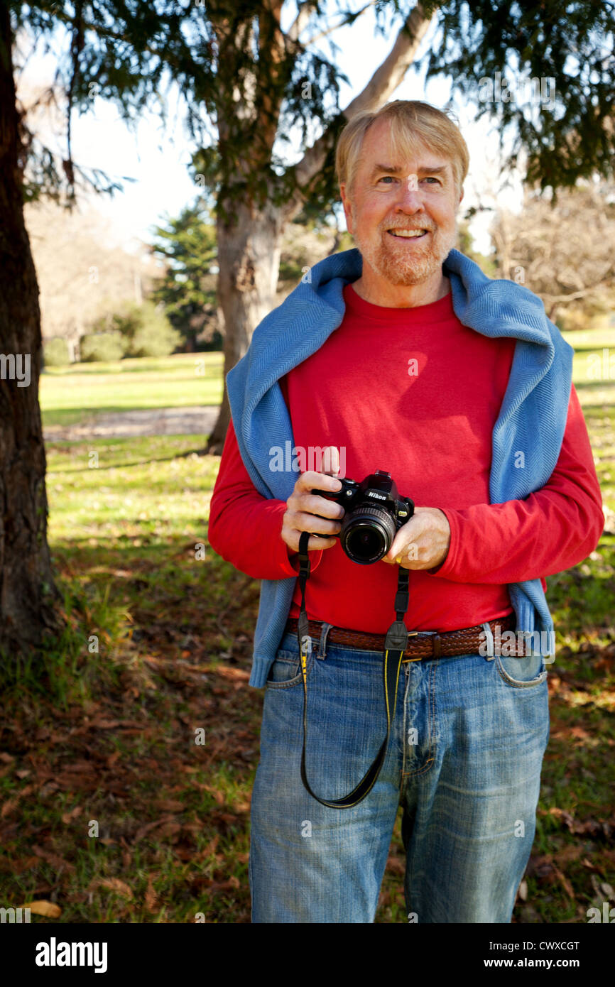 Un homme dans son 60's est debout à l'extérieur tenant une caméra. Banque D'Images