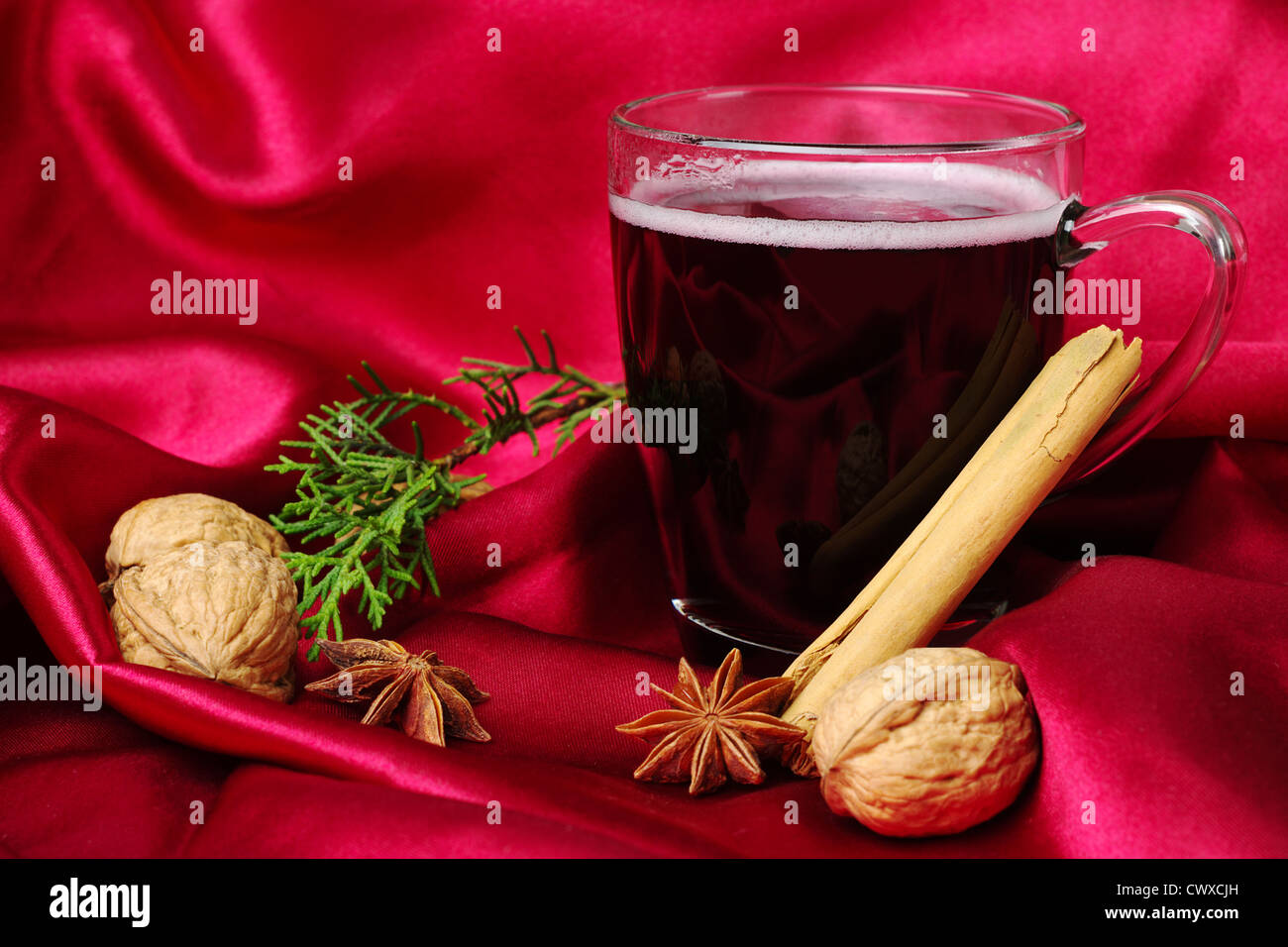 Vin rouge épicé chaud avec de la cannelle, de la badiane, noix et une branche d'evergreen sur fond rouge (Selective Focus) Banque D'Images