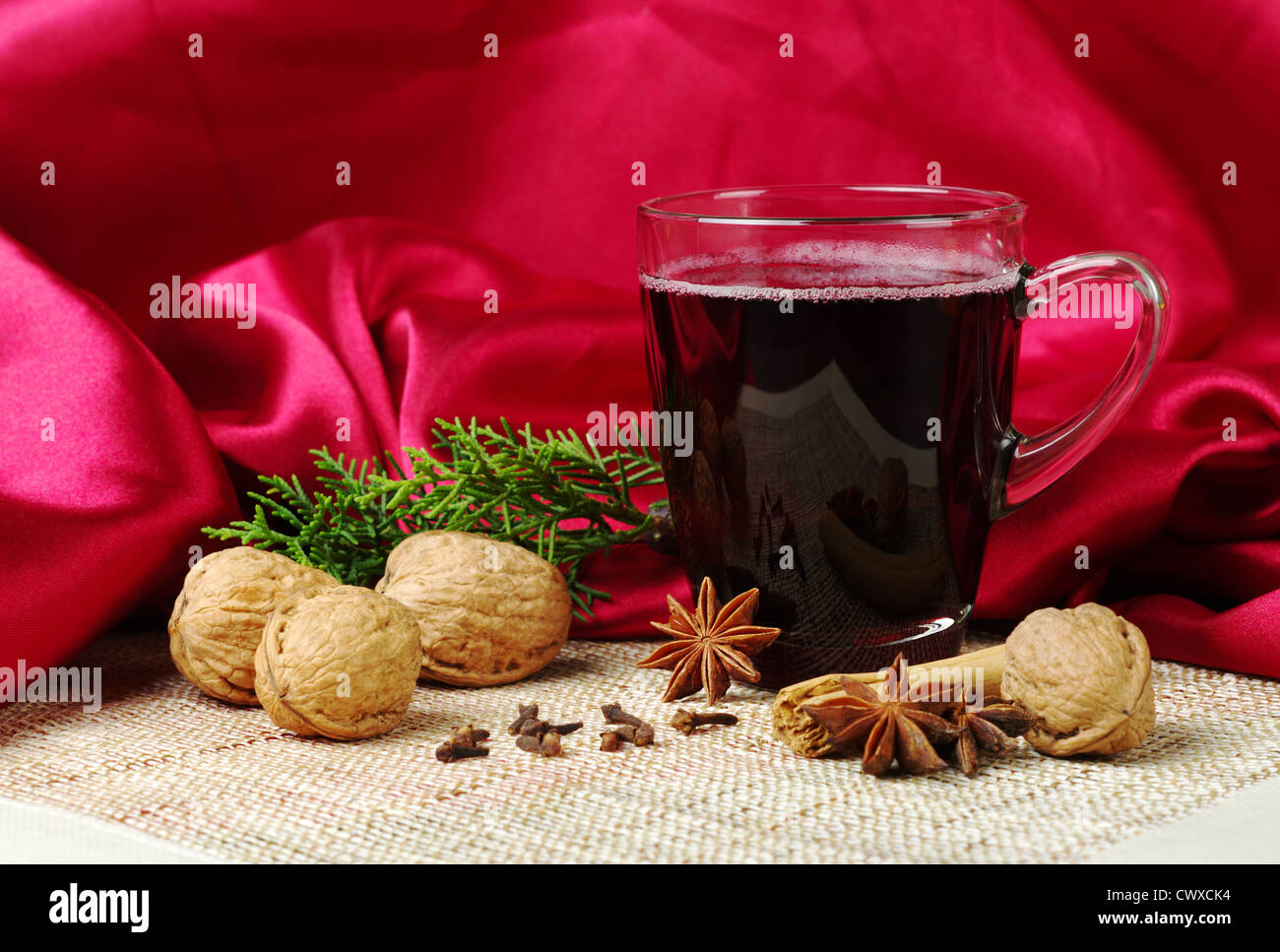 Vin chaud à la cannelle, badiane, girofle, noix et une branche d'evergreen sur tapis avec tissu rouge en arrière-plan Banque D'Images