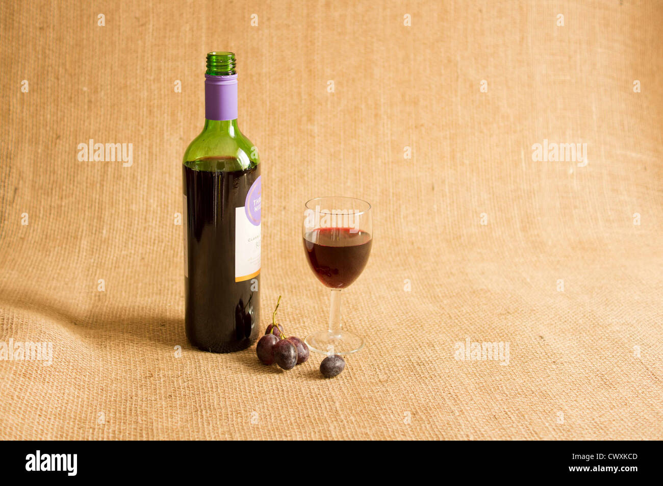Ouvre bouteille de vin rouge avec un verre de vin à moitié rempli de raisins rouges sur un fond de toile de jute. Banque D'Images