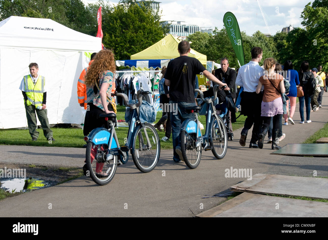 Les femmes et l'homme poussant Barclay's Bikes along path at Camden Londres maintenant juste vert, England UK Banque D'Images