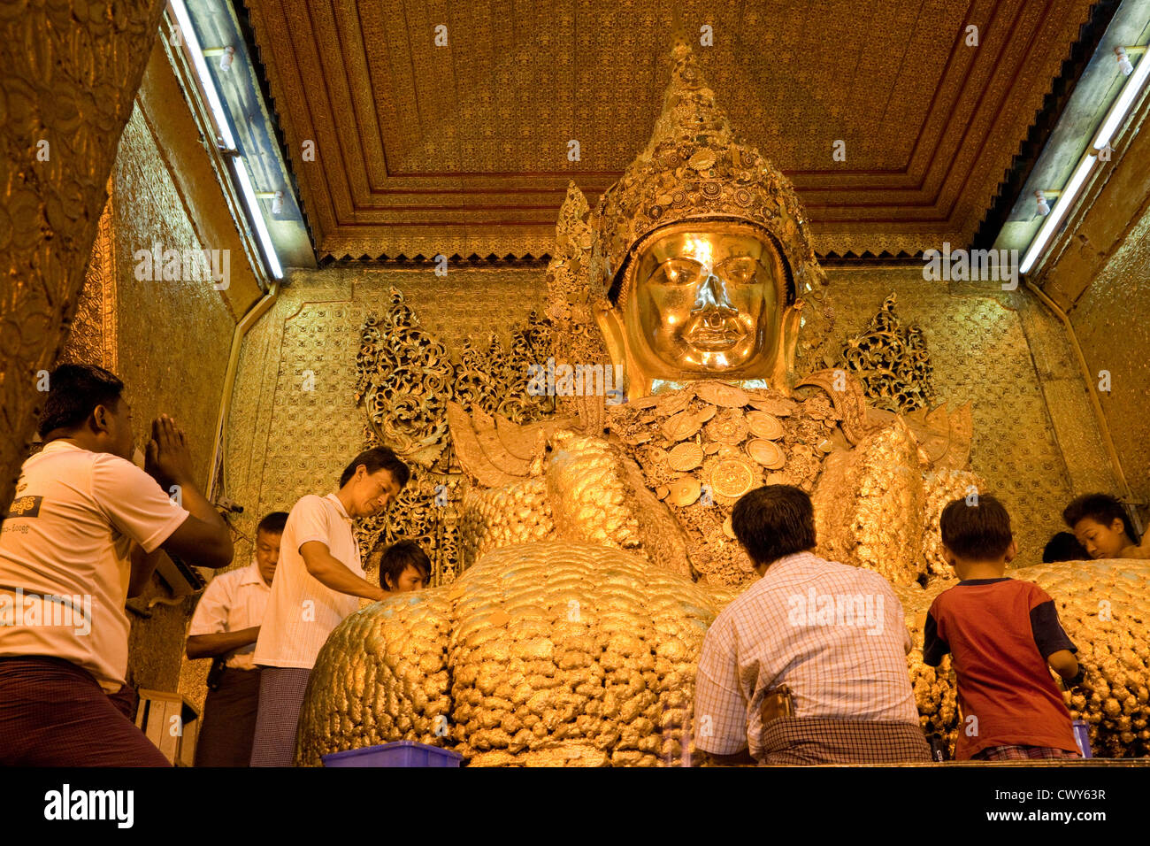 Le Myanmar, Birmanie. Mandalay. Temple bouddhiste de Mahamuni. Les hommes et les garçons s'appliquer de la feuille d'or de statue de Bouddha. Banque D'Images