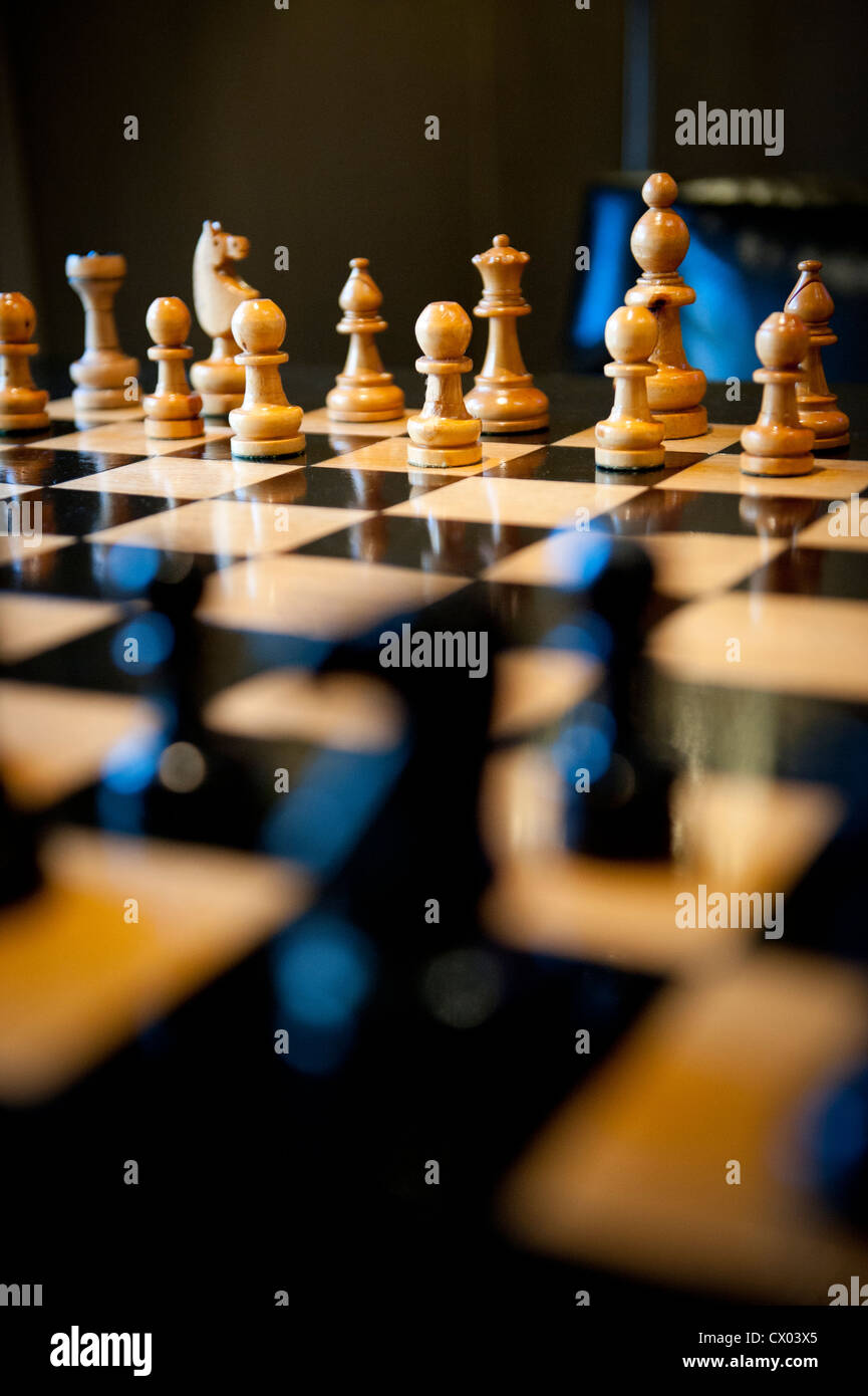 Pièces des échecs en bois sculpté sur un échiquier de lumière chaude. Banque D'Images