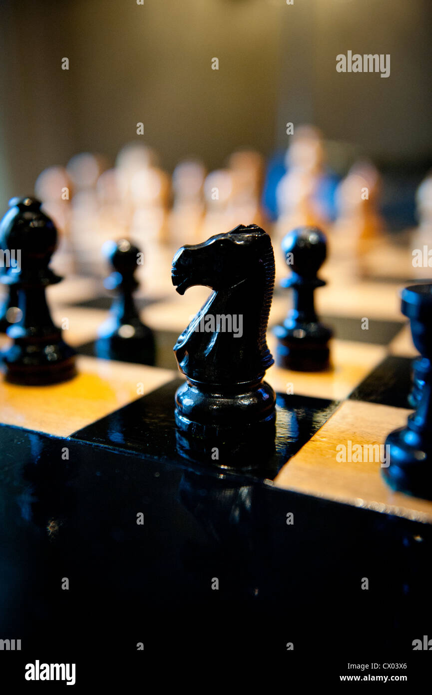 Pièces des échecs en bois sculpté sur un échiquier de lumière chaude. Banque D'Images