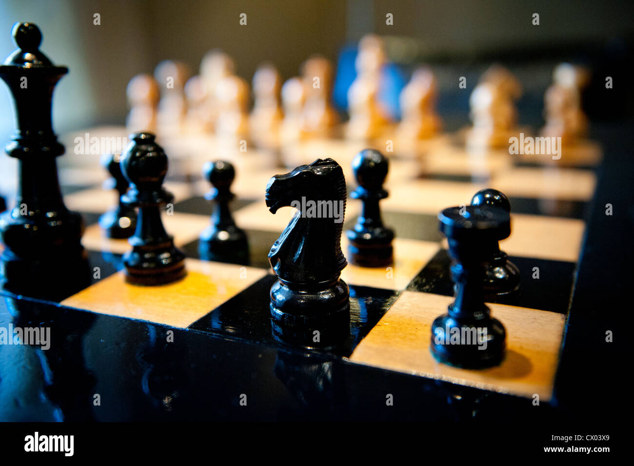 Pièces des échecs en bois sculpté sur un échiquier de lumière chaude. Banque D'Images