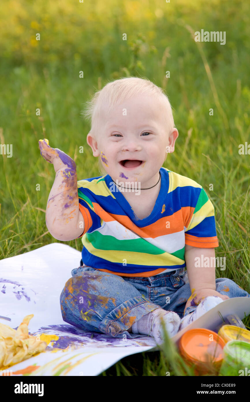 Petit bébé garçon avec le syndrome de peinture Les peintures au doigt sur du papier blanc avec un sourire. Le bonheur est dans la créativité. Banque D'Images