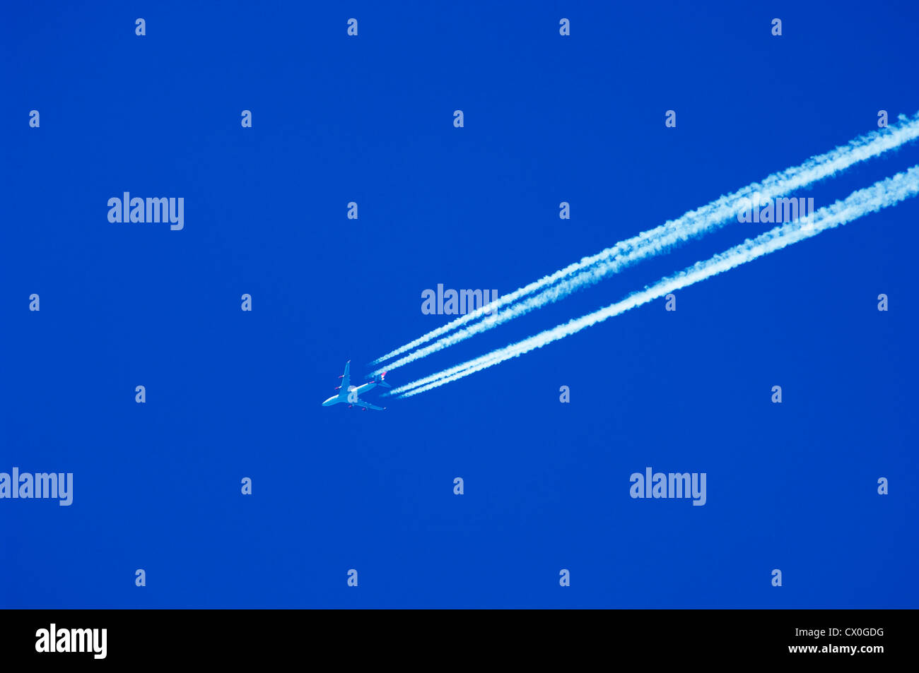 Un jet de passagers volant à haute altitude en laissant des traînées de vapeur contre un ciel bleu clair. Banque D'Images