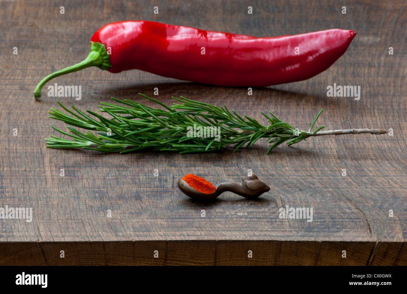 Poivron rouge frais, branche de romarin, cuillère de mesure de piment rouge moulu spice sur dark, planche à découper en bois. Banque D'Images