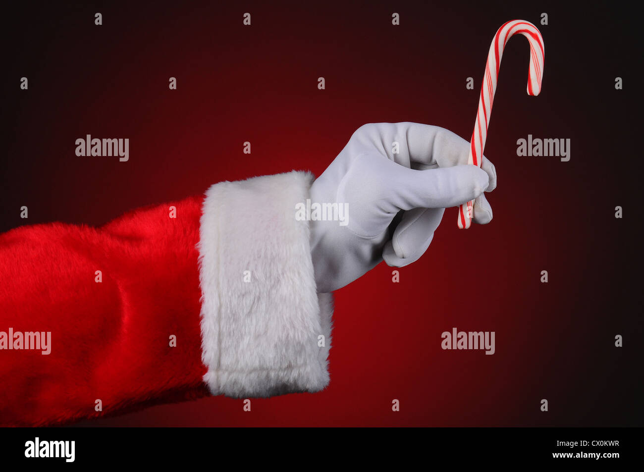 Santa Claus main tenant une canne sur un feu rouge à l'arrière-plan sombre. Format horizontal montrant seulement des mains et des bras. Banque D'Images