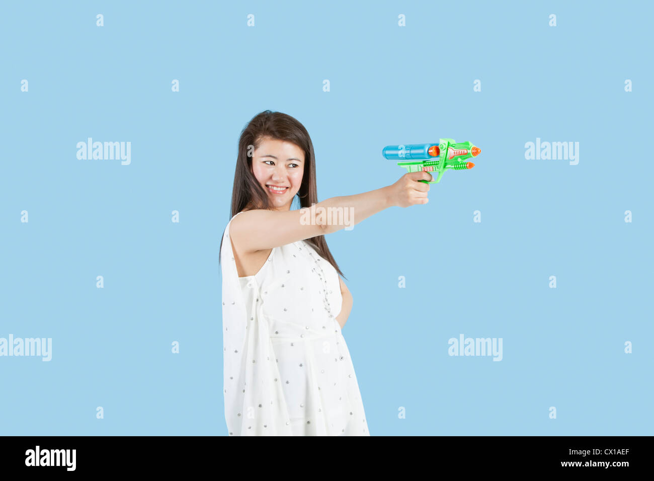 Happy young woman visant avec un pistolet jouet sur fond bleu Banque D'Images