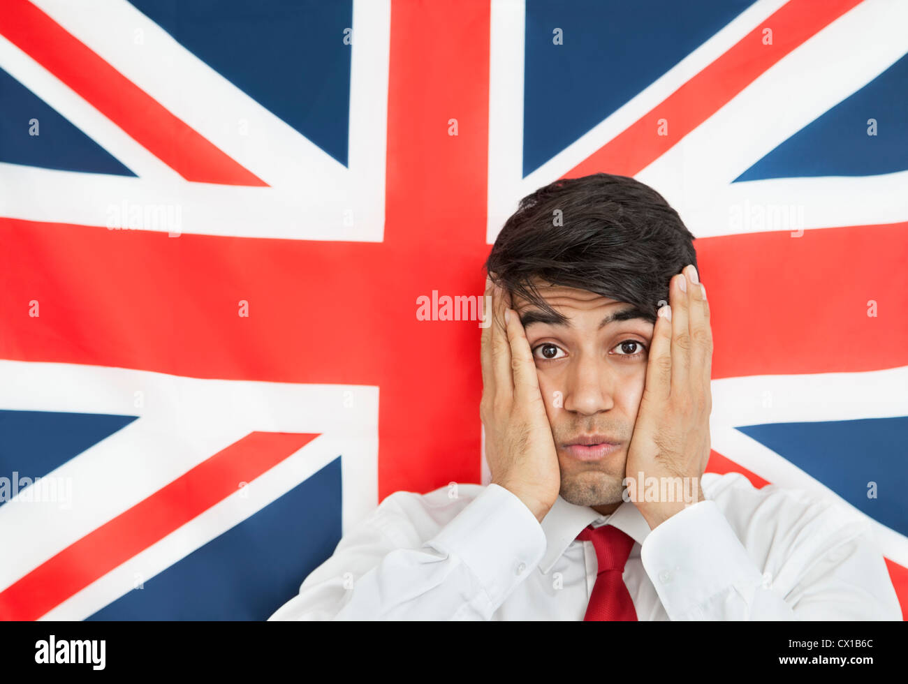 Portrait d'un homme Indien choqué avec les mains sur les joues contre drapeau britannique Banque D'Images