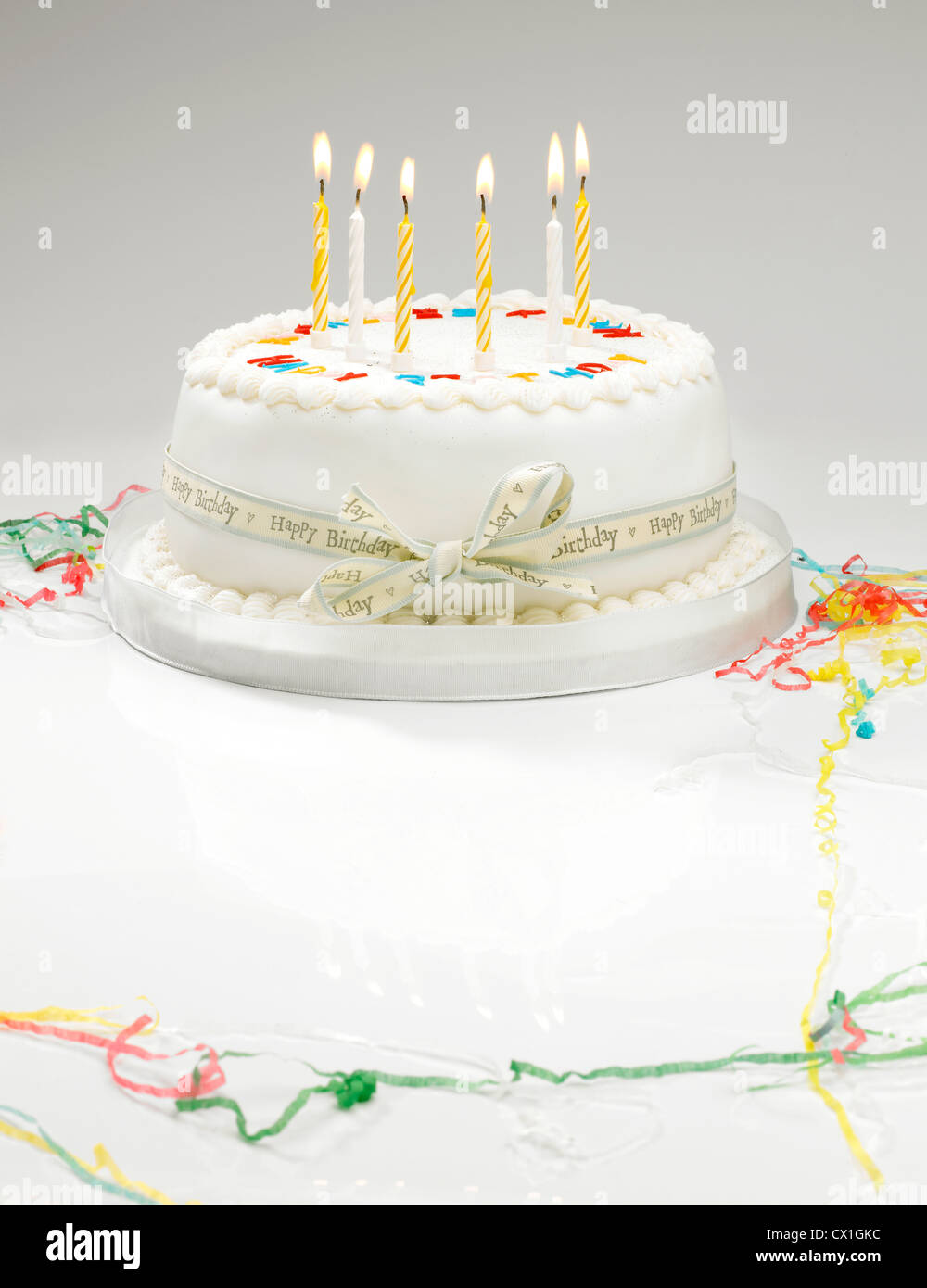 Un gâteau d'anniversaire blanche avec la lumière des bougies et de banderoles Banque D'Images