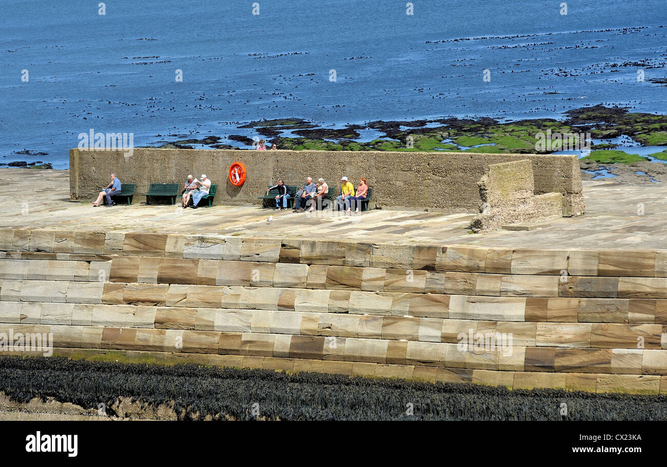 Les touristes assis sur la jetée est à Whitby, North Yorkshire angleterre uk Banque D'Images