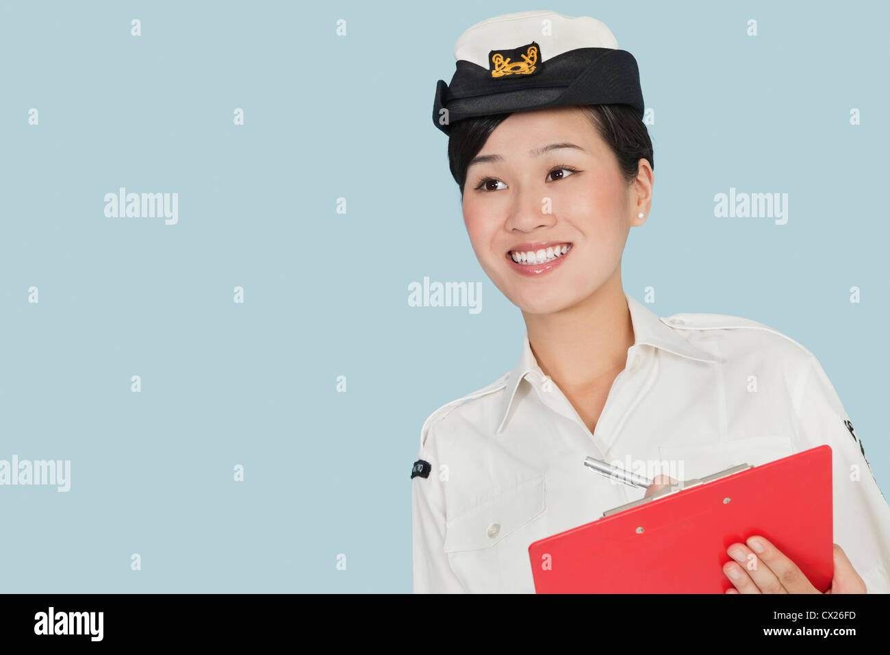 Happy female US Navy officer with clipboard smiling over light blue background Banque D'Images