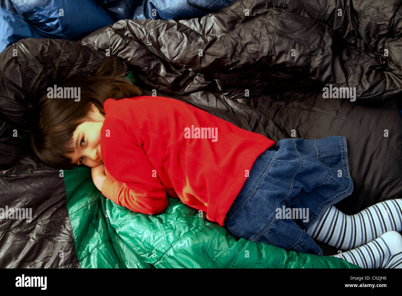 Petite fille couchée sur certains sacs de couchage dans une tente. Banque D'Images