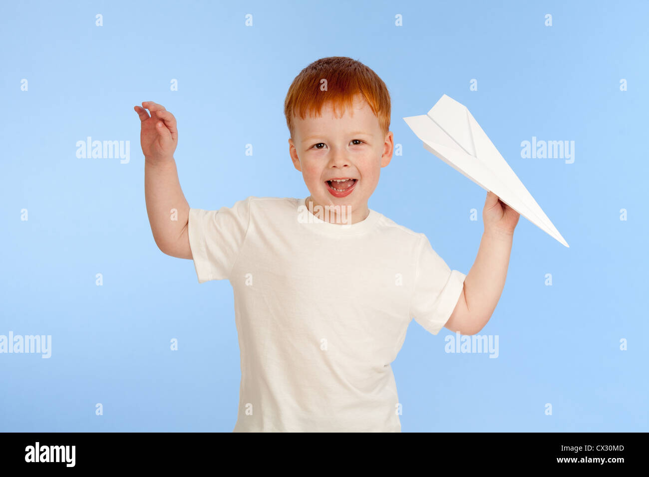 Adorable garçon roux avec paper plane modèle sur fond bleu en studio Banque D'Images