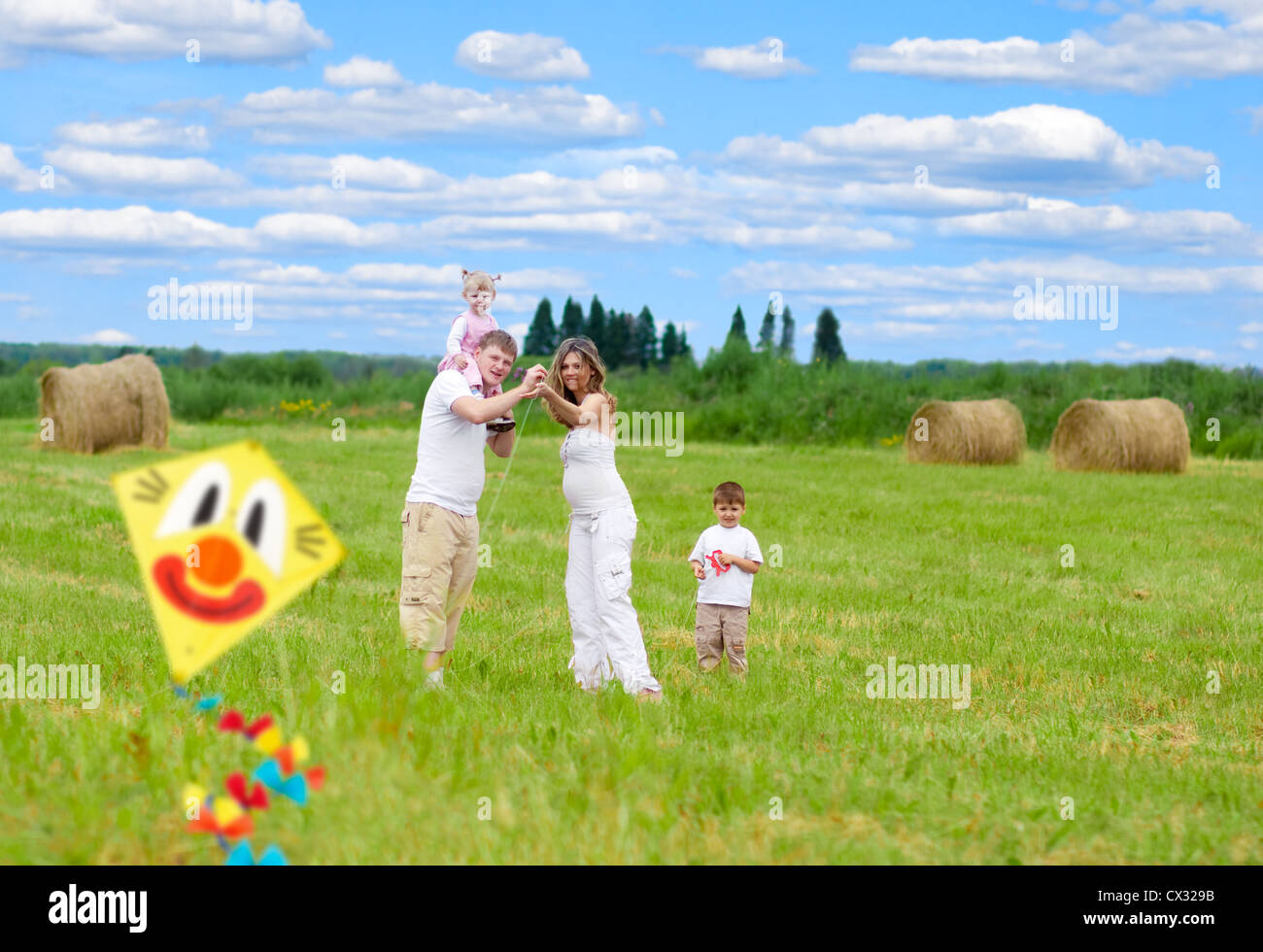 Famille heureuse avec femme enceinte en vol d'un cerf-volant en champ d'été ensemble Banque D'Images