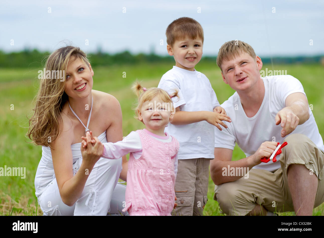 Famille heureuse avec femme enceinte en vol d'un cerf-volant en champ d'été ensemble Banque D'Images