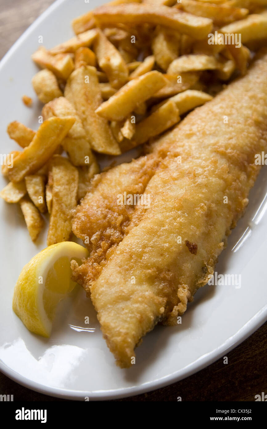 Plaque blanche of battered fish and chips avec tranche de citron sur la table Banque D'Images
