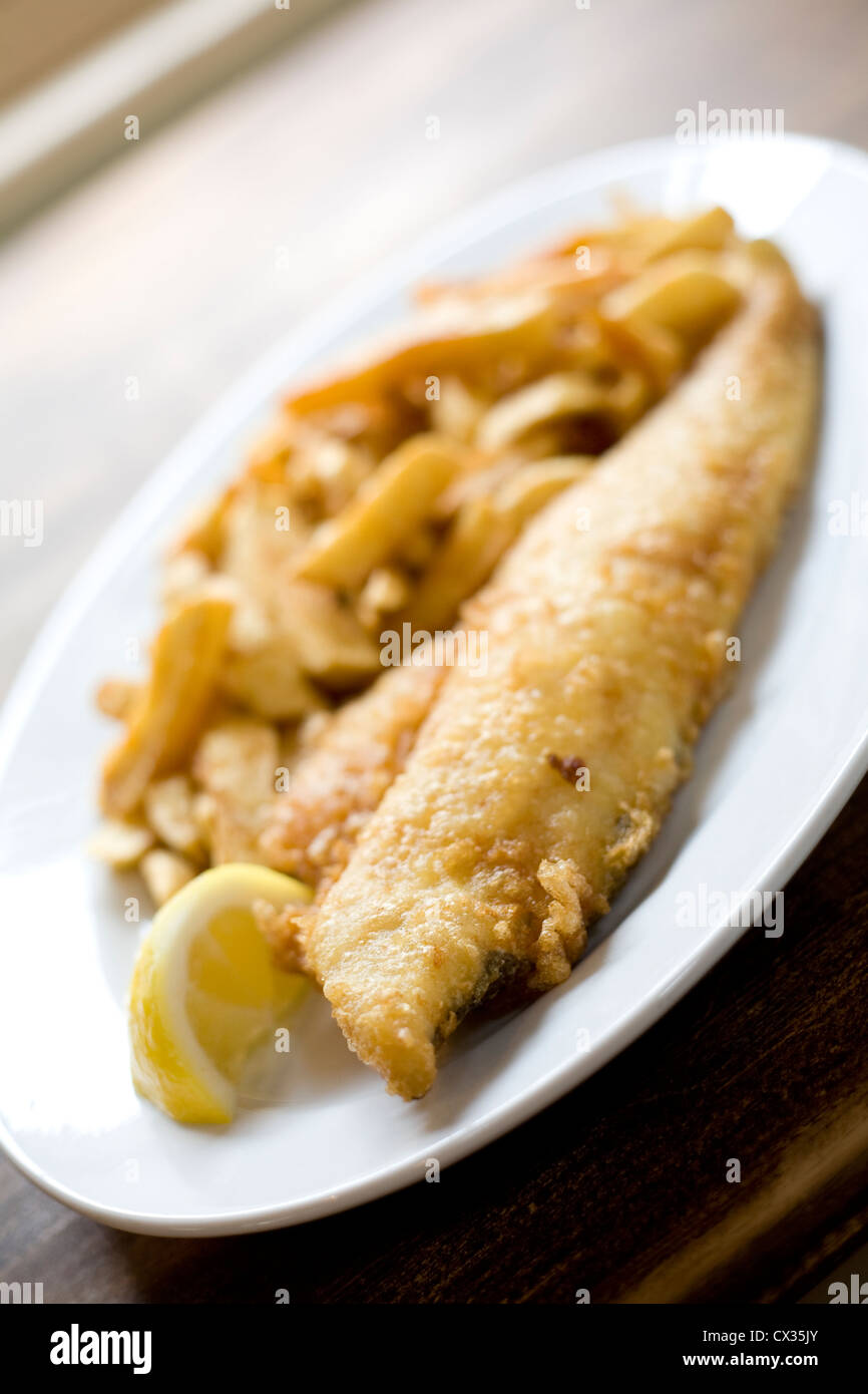 Plaque blanche of battered fish and chips avec tranche de citron sur la table Banque D'Images