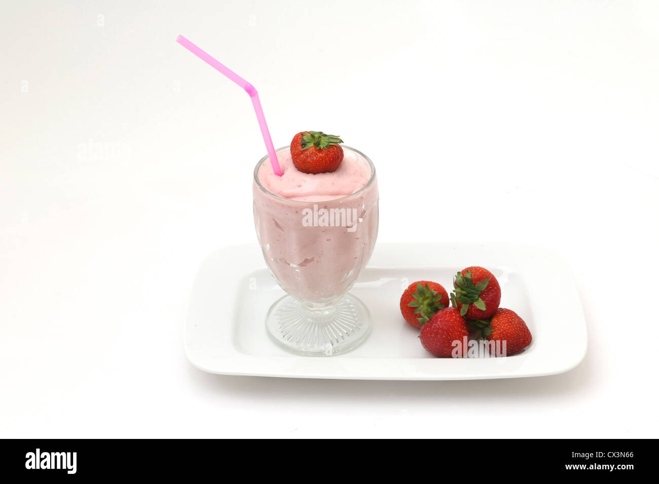 Lait frappé aux fraises dans un verre avec des fraises sur un plat et deux pailles Banque D'Images
