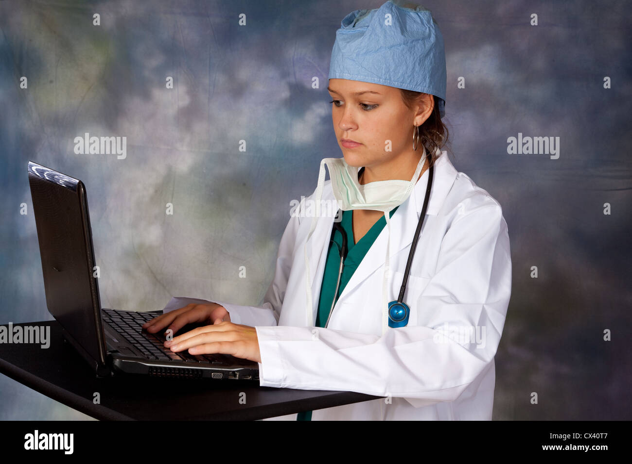 Travailleur de la santé des femmes, portant un sarrau blanc, scrub hat et stéthoscope autour du cou, de la saisie sur un ordinateur portable Banque D'Images