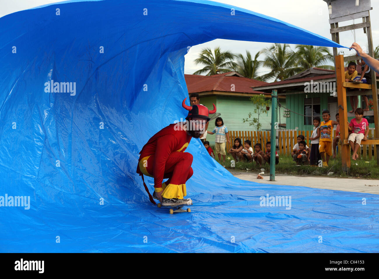 Fou barbu en rouge costume de super-héro d'effectuer une démonstration de surf de bâches pour les villageois sur une planche à roulettes. Banque D'Images